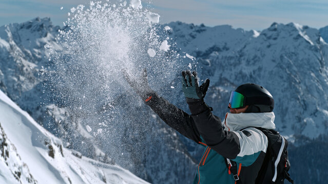 Close-up of a skier throwing fresh snow into the air with gloved hands, capturing a playful winter sports moment with flying snow, alpine adventure, energy, and the joy of skiing.