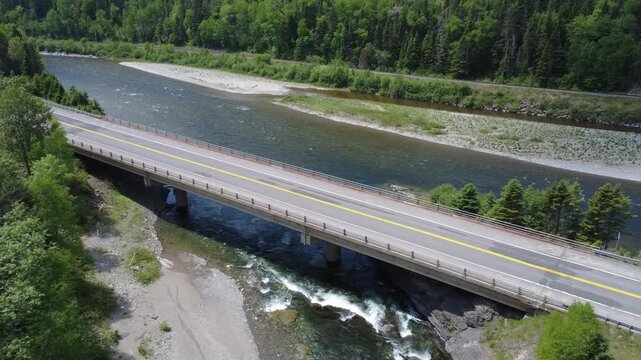 Drone footage descends toward the concrete pillars of a road bridge crossing the Assemetquagan River near its confluence with the Matapedia River in Saint-Andr&eacute;-de-Restigouche, Quebec.