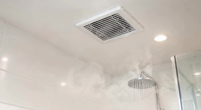 Steam rising from a running rain shower under a ceiling exhaust fan in a modern tiled bathroom with glass enclosure and recessed light
