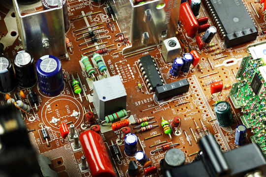 Complex electronics hardware fills printed circuit board, featuring colorful resistors, capacitors, microchips, solder joints and metal parts in intricate closeup of technical electronic assembly