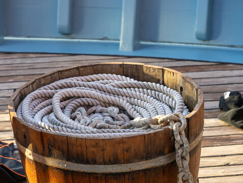 Coiled Nautical Rope and Anchor Chain in Rustic Wooden Barrel on Historic Ship Deck