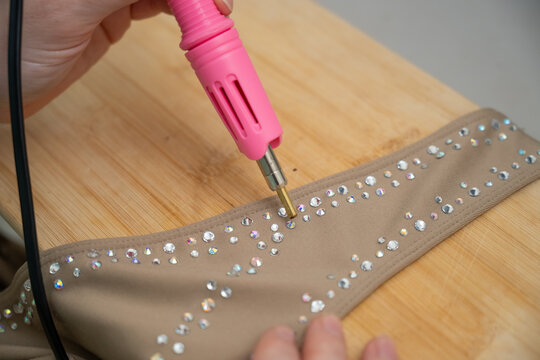 A woman glues rhinestones onto a gymnastics costume using a soldering iron. Hot fix.