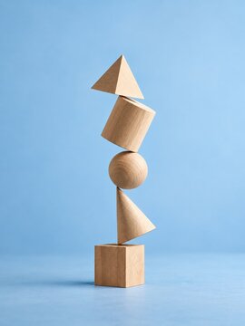 Wooden geometric solids stacked in a precarious vertical tower, featuring smooth natural textures on a light blue background for business and strategy
