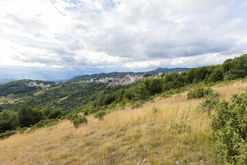 Fototapeta premium Mountain resort surrounded by forested hills under dramatic clouds