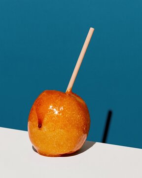 Golden orange toffee apple with a glossy sugar glaze and red drip on a teal background, featuring copy space for seasonal shopping