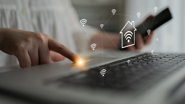 A person interacts with a laptop, using a smartphone in a modern home setting, showcasing the blend of digital technology and smart home connectivity. Gantry