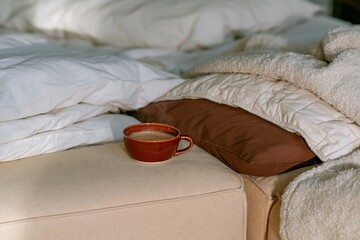 Obraz premium Coffee cup steaming on a yellow sofa arm beside plush cushions and a throw blanket, a cozy home scene for relaxation and autumn breaks