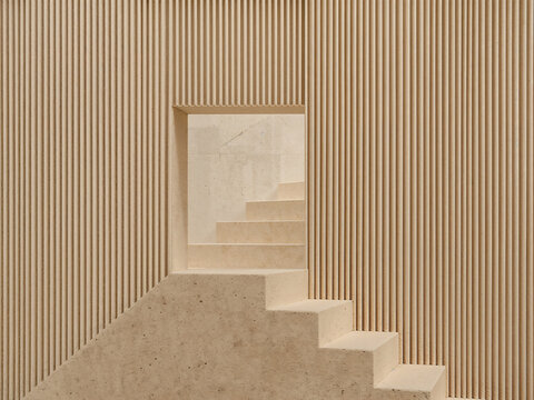A beige stone staircase leading through a rectangular opening in a wall with vertical ribbed paneling, creating a minimalist architectural scene