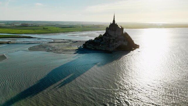 Long shadow of Mont Saint Michel across tidal flats in Normandy, France. Aerial footage of medieval island abbey with pronounced shadow