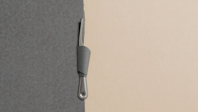 Silver metal tool with a grey handle placed on a split background, of dark grey, and beige paper, minimalist view of, stationery equipment