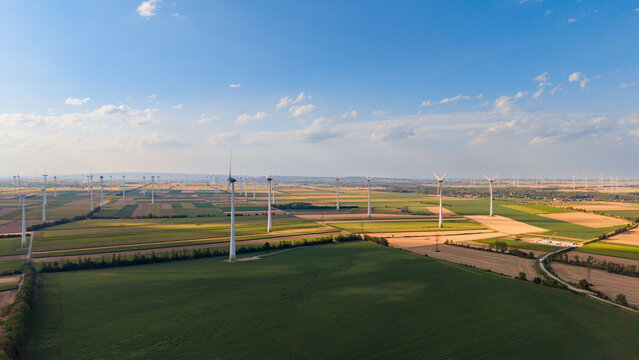 Aerial view of wind turbine farm across farm fields. High angle perspective showing multiple wind turbines scattered across patchwork agricultural fields.