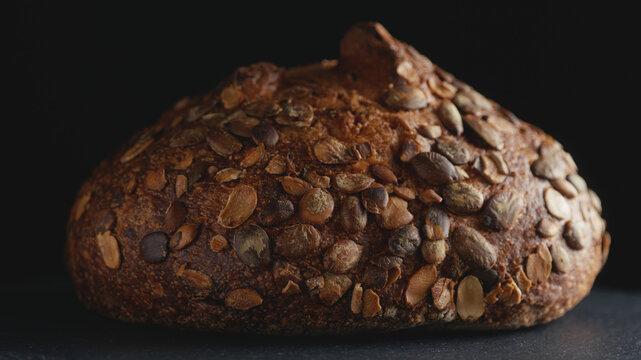 Close-up of artisan whole wheat sourdough bread topped with pumpkin seeds on a dark background. Freshly baked organic loaf with crispy crust for commercial bakery promotions and healthy food concept.
