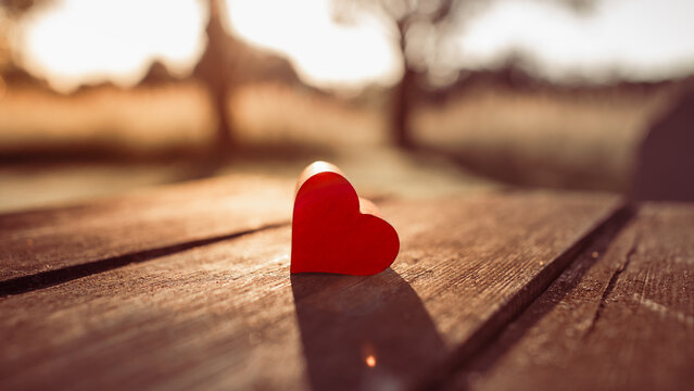Red heart on wooden table in warm sunlight symbolizing love, romance, compassion and connection