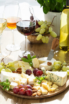 Assortment of fine cheeses with red and white wine and fresh grapes presented on a wooden platter