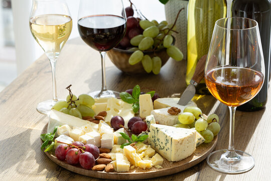 Appetizing cheese platter with red and white wine assortment and grapes on rustic wooden table