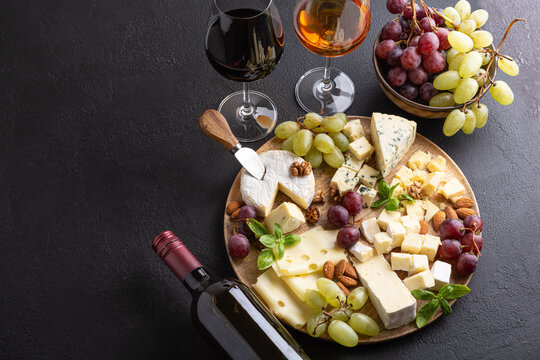 Assortment of cheeses, grapes, nuts, and wine bottle presented on a dark textured surface