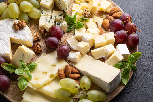 Assortment of fine cheeses grapes nuts and basil leaves on wooden board