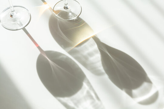 Abstract light patterns cast by wine glasses creating minimalist composition on white surface