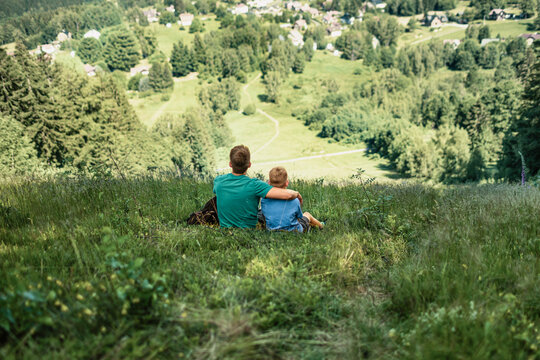 Father and son relaxing together on mountain hillside, fatherhood, parenting, family bonding, support and outdoor adventure concept
