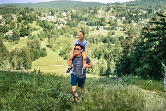 Father carrying daughter on shoulders while hiking in mountains, family adventure, fatherhood, childhood, outdoor activity and bonding concept
