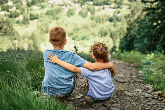 Brother and sister child friends embracing while sitting together on mountain trail, sibling love, childhood friendship, family bond, support and adventure concept
