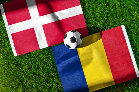 Denmark vs. Romania football match. National flags on green grass with soccer ball in the middle. Football background for international match.