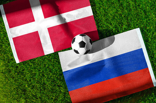 Denmark vs. Russia football match. National flags on green grass with soccer ball in the middle. Football background for international match.