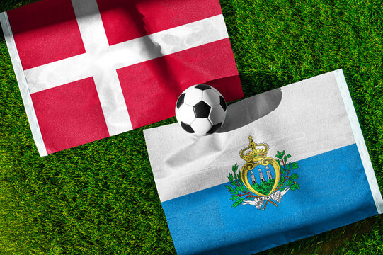 Denmark vs. San Marino football match. National flags on green grass with soccer ball in the middle. Football background for international match.