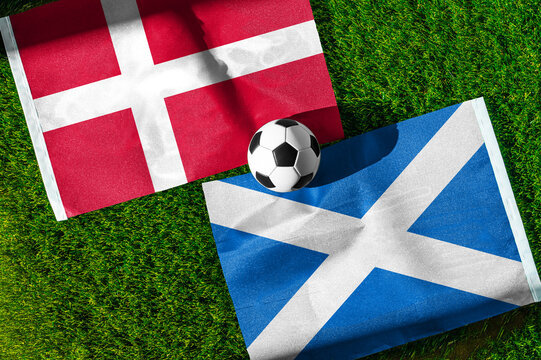 Denmark vs. Scotland football match. National flags on green grass with soccer ball in the middle. Football background for international match.