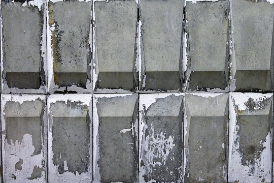 Horizontal photo of a weathered concrete panel wall with a repeating geometric diamond relief pattern.