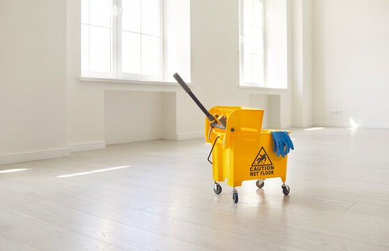 Caution wet floor sign with equipment and supplies in empty room for cleanup. Cleaning service and housekeeping concept. Safety warning stand to reduce risk of dangerous fall, preventing accidents 