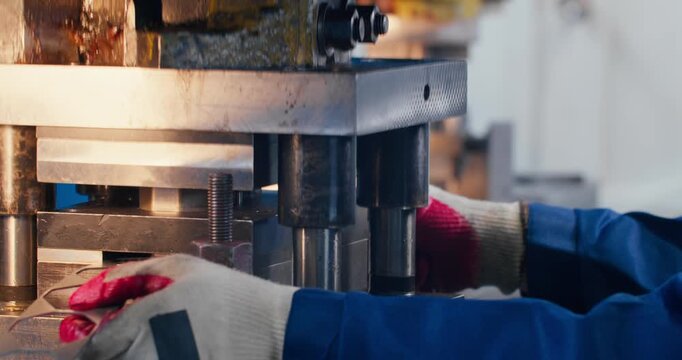 Metalworking shop floor with factory worker operating mechanical press. Close-up of metal stamping and blue collar manufacturing work