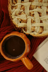 Obraz premium Homemade apple pie with a lattice top next to a cup of hot coffee and an open book, autumn leaf decor, cozy autumn reading setting, film grain effect, high-quality photo