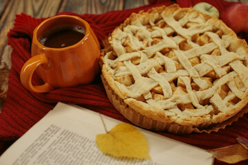 Obraz premium Homemade apple pie with a lattice top next to a cup of hot coffee and an open book, autumn leaf decor, cozy autumn reading setting, film grain effect, high-quality photo