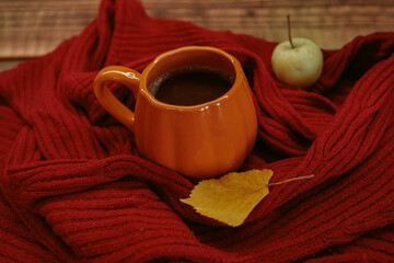 Obraz premium An orange mug of coffee resting on a red knitted sweater beside an open book and a yellow autumn leaf, with soft film grain, high quality photo