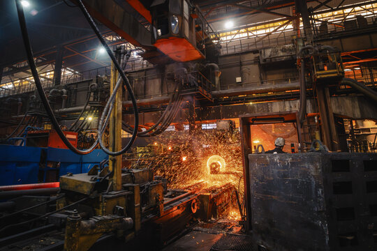 Centrifugal casting of ductile iron pipe with glowing metal and flying sparks inside heavy foundry manufacturing line.