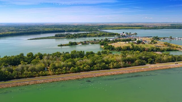 Embankment road along water reservoir. Aerial shot displays paved road running along stone reinforced bank bordering green water.