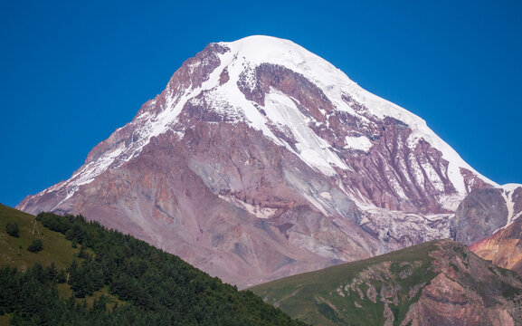 Mount Kazbek snow covered summit above Stepantsminda, Georgia, majestic Mkinvartsveri peak in Caucasus mountain landscape under clear blue sky.