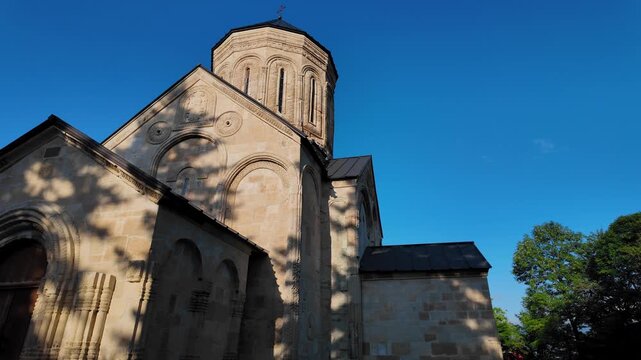 Stone facade of the medieval nikortsminda cathedral, an important monument of georgian architecture, with its intricately carved dome highlighted by the morning sun against a clear blue sky