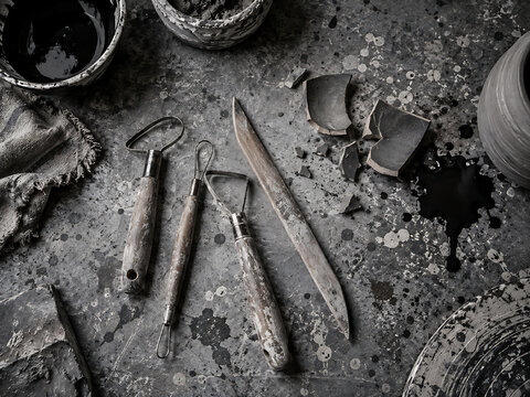 Pottery tools and broken ceramic pieces on a textured gray surface dark moody still life