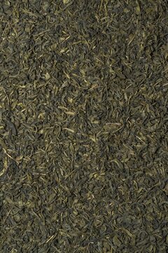 Close-up texture of loose dried green tea leaves with natural earthy tones and detailed organic patterns.