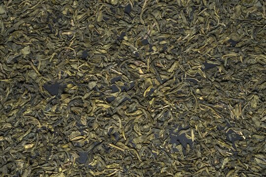 Close-up texture of loose dried green tea leaves with natural earthy tones and detailed organic patterns.