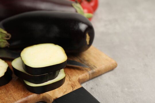 Fresh raw eggplants, board, knife and tomatoes on light grey table, closeup. Space for text