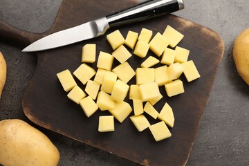 Fototapeta premium Cutting board with pieces of raw young potatoes and knife on grey table, flat lay