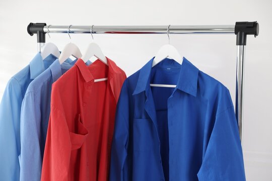 Different shirts hanging on rack near white wall indoors, closeup