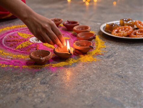 Woman lighting traditional clay diyas for Diwali festival with colorful rangoli and sweets on floor
