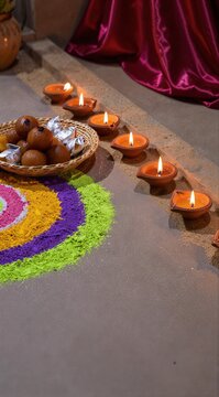 Diwali celebration with illuminated clay lamps diyas, colorful rangoli powder art, and sweets gulab jamun in a basket for traditional Indian festival