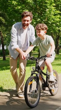 Father teaches young boy cycling on bright riverside path
