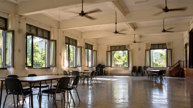 Spacious empty community hall interior with ceiling fans large open windows and tables. Concept of assembly hall, empty room. Copy space.