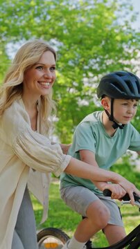Mother guides boy riding bicycle during sunny park practice